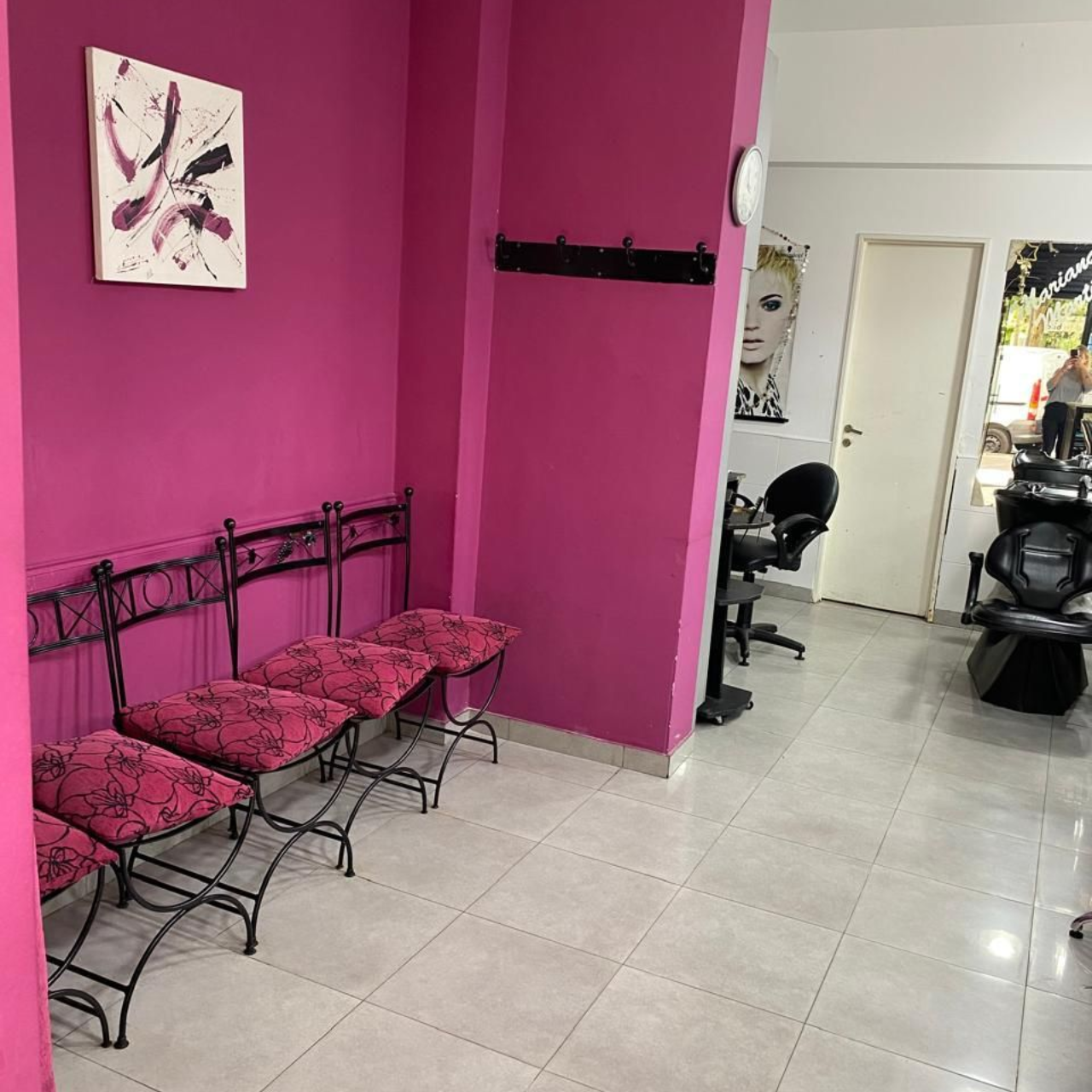 Una sala de espera de salón de belleza con paredes rosas, sillas y arte.