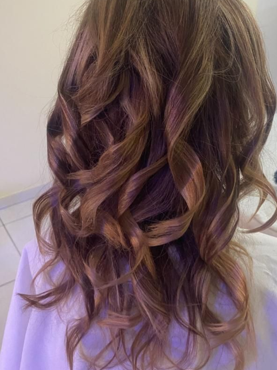 Cabello castaño hasta los hombros con reflejos castaños claros, peinado con rizos sueltos y definidos.