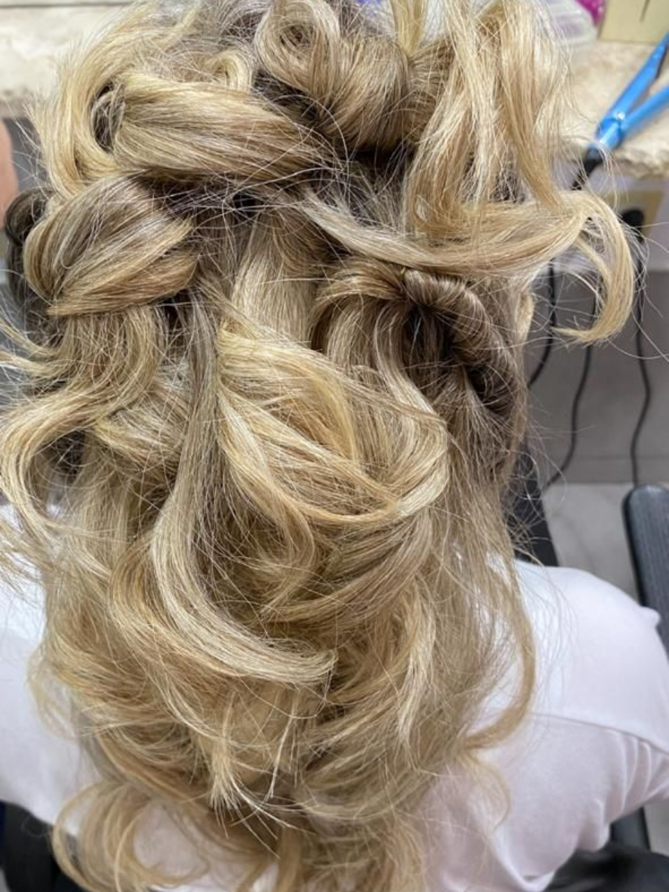 Peinado recogido rubio y rizado con giros y mechones sueltos, posiblemente para un evento formal.