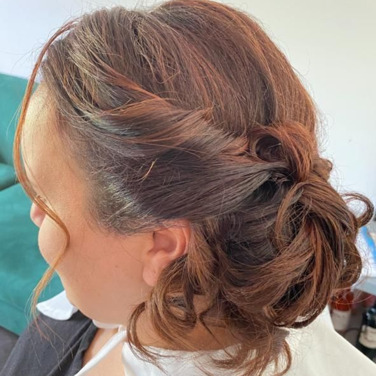 Mujer con peinado recogido color castaño rojizo, con trenza lateral retorcida y moño bajo, en interiores.