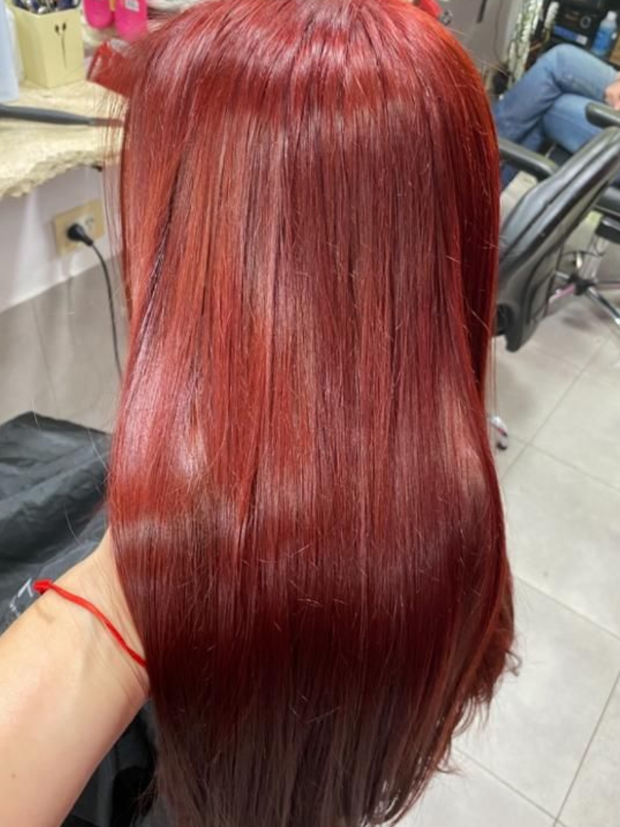Cabello rojo, liso y brillante, sostenido en la mano en un salón.