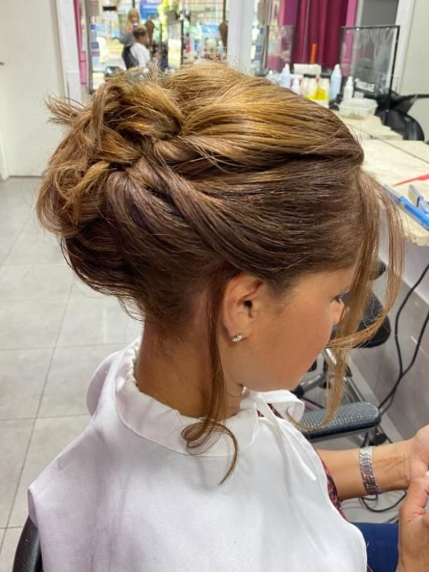 Mujer con peinado recogido en un salón, con cabello castaño retorcido y recogido, vista lateral.