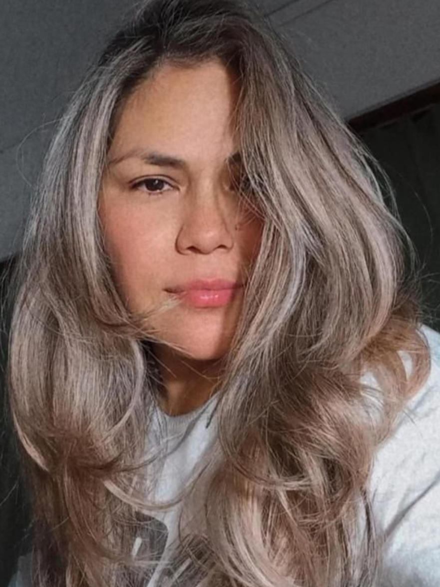 Mujer con cabello largo, ondulado, gris y rubio, mirando a la cámara.