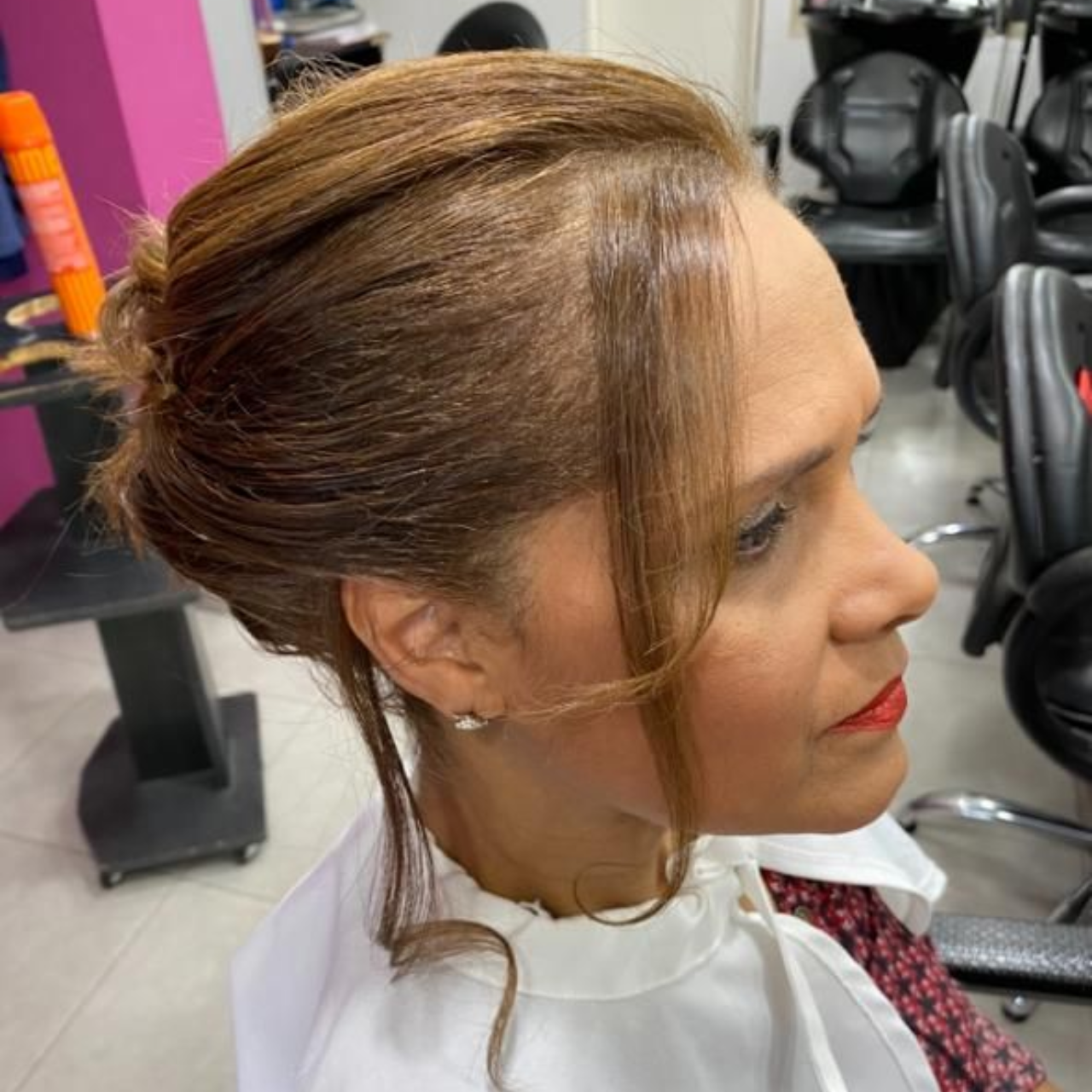 Mujer con peinado recogido en un salón; vistiendo una capa blanca.