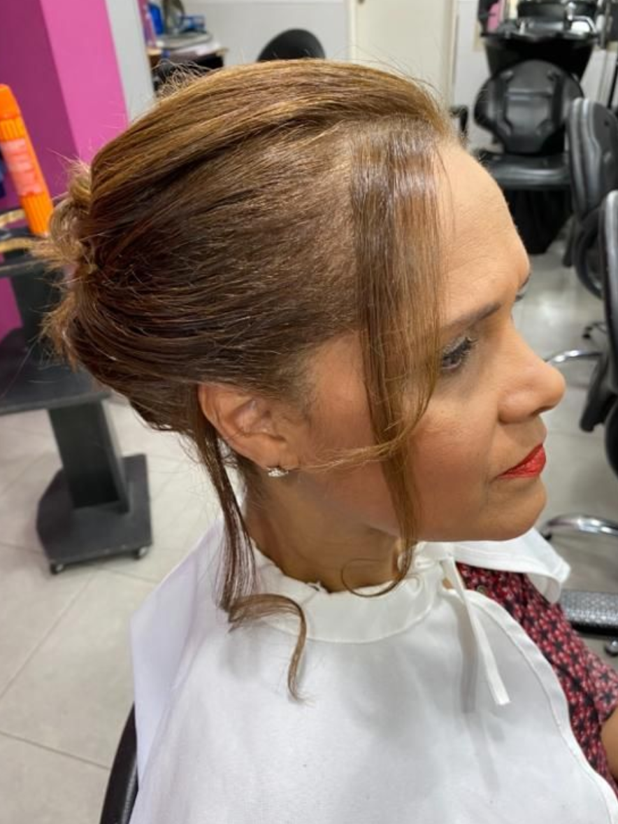 Mujer con peinado recogido en el salón, con capa blanca, vista de perfil.