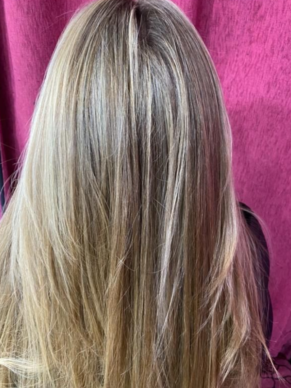 Cabello rubio con reflejos, en capas y liso, sobre un fondo rosa.