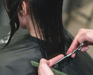 Peluquero cortando el cabello oscuro y mojado de una clienta con tijeras y un peine en un salón.