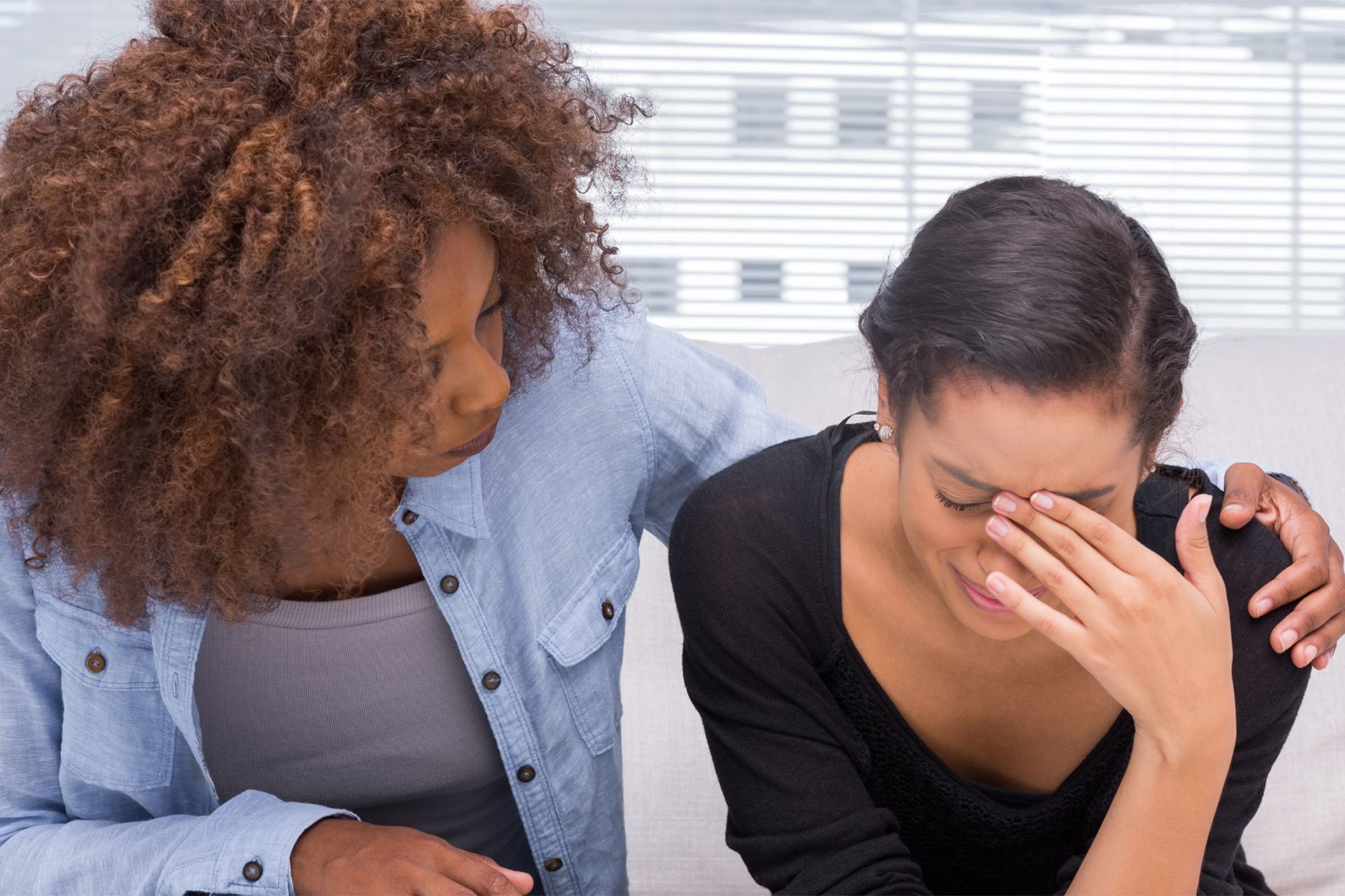 A woman is comforting another woman who is crying on a couch.