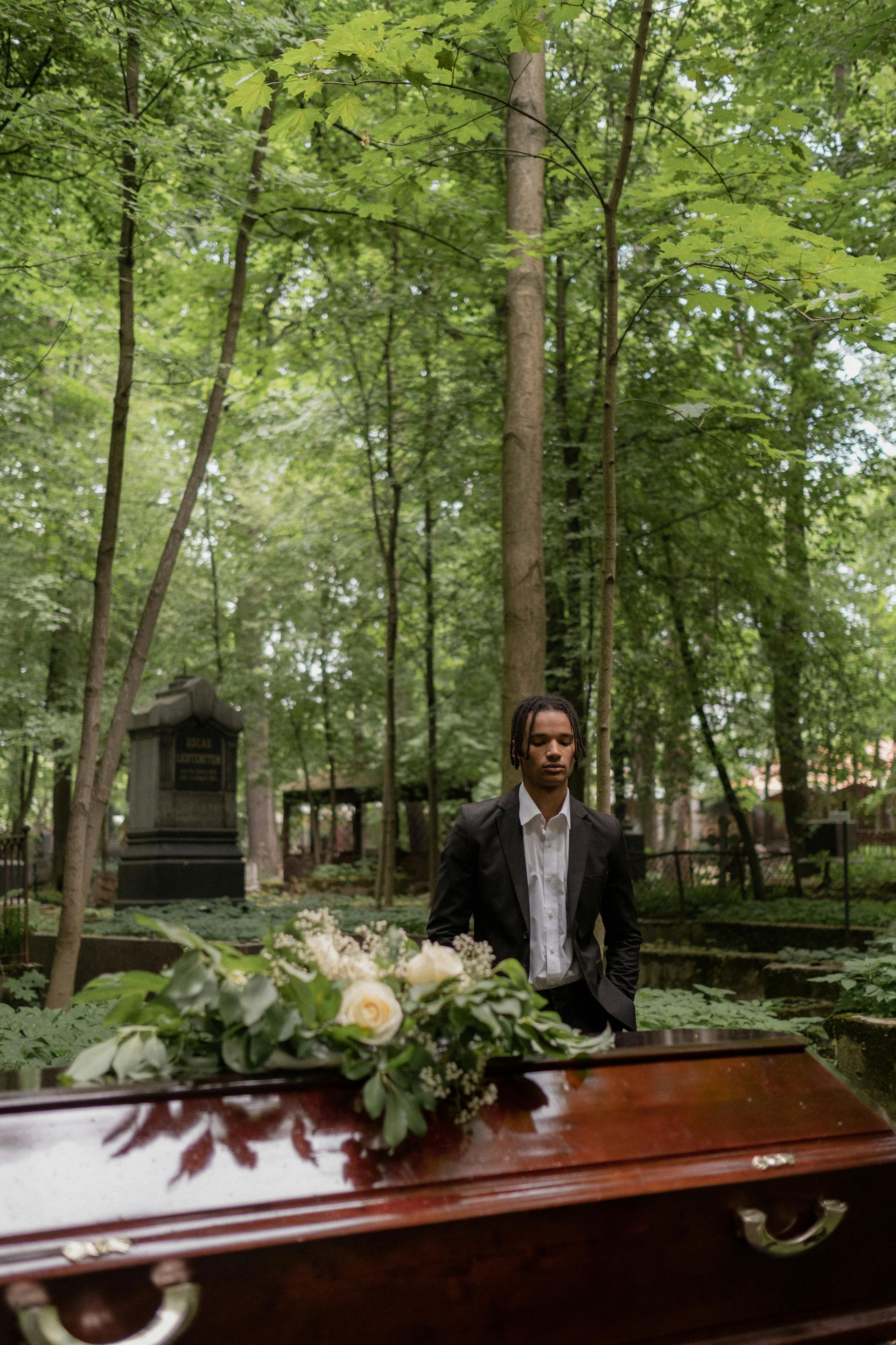 A man in a suit is standing next to a coffin in a cemetery.