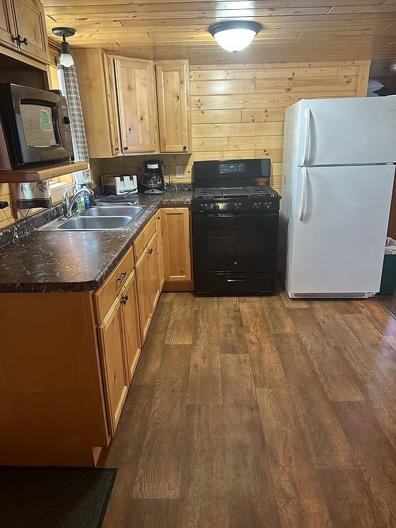 A cabin kitchen featuring wooden cabinets, black appliances, and a white refrigerator.