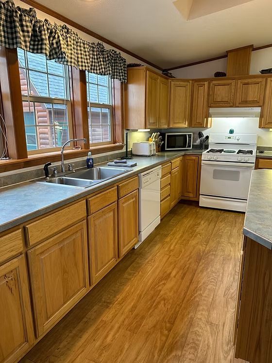 Kitchen with wood cabinets, white appliances, and a window with a checkered valance.