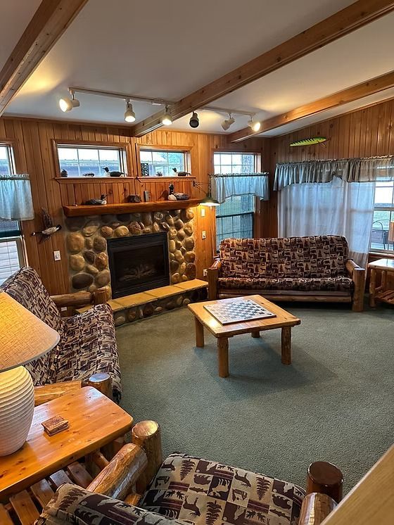 Living room with stone fireplace, wood furniture, and green carpet.