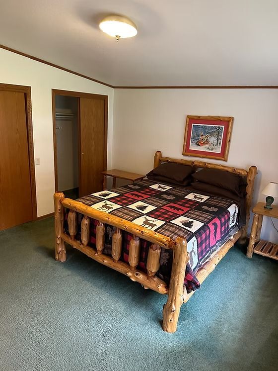Bedroom with a log bed, patterned quilt, two closets, and green carpet.