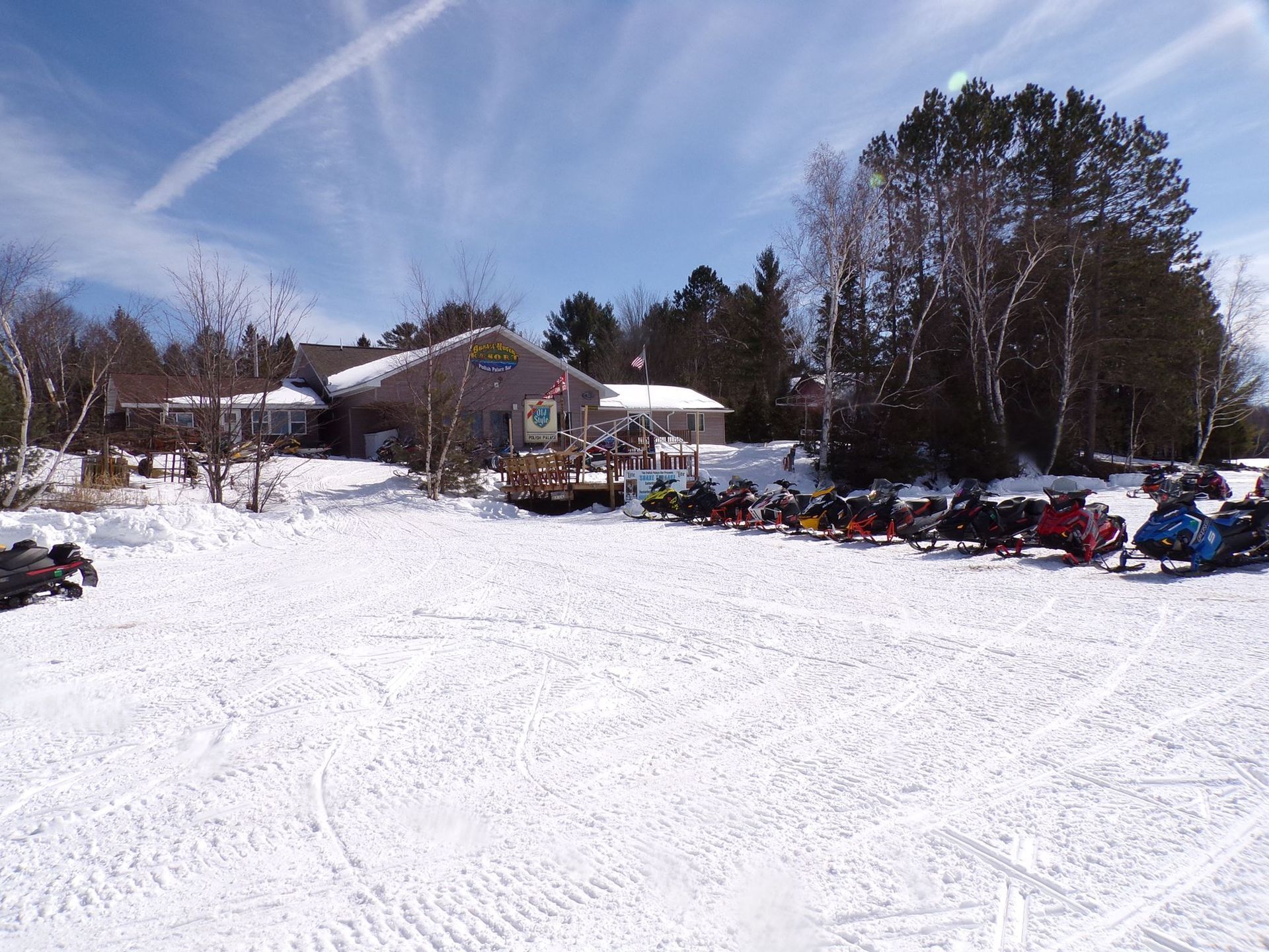 Snow-covered landscape with a building and parked snowmobiles. Sunny, blue sky.