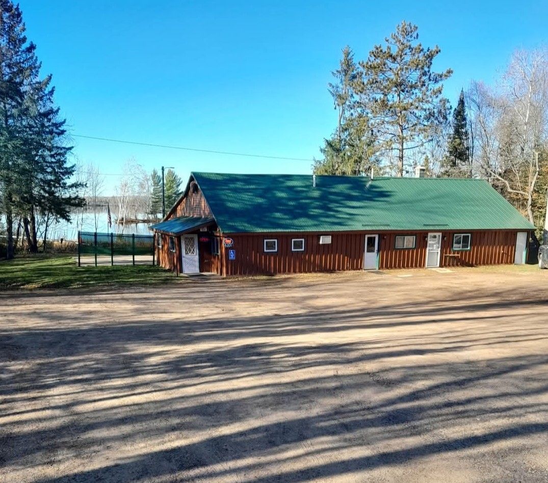 Brown wooden building with green roof, several white doors, and a lake in the background.