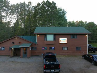 Exterior of a brown two-story building with a sign, cars parked out front, and trees in the background.