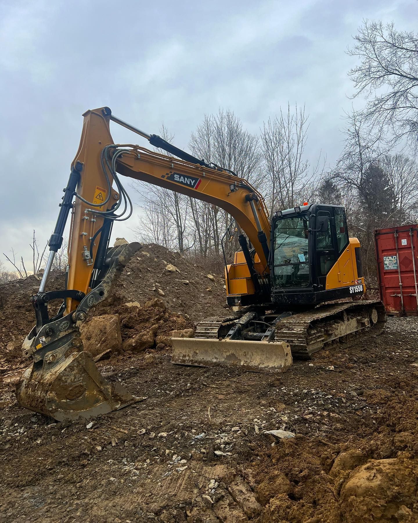 A yellow excavator is sitting in a dirt field next to a red container.