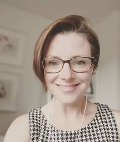 A woman wearing glasses and a black and white dress is smiling.