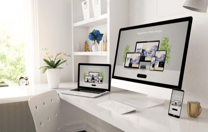 Web design mockups on a computer, laptop, and phone; a desk with a white chair and window.