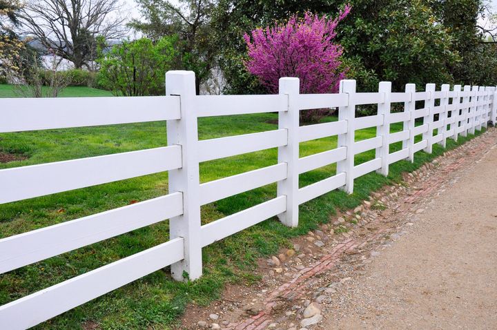 White wooden ranch rail fence along a green yard.