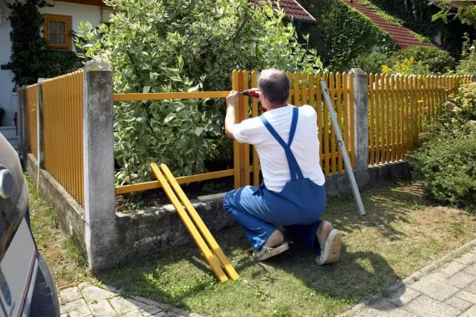 Contractor building a yellow wooden picket fence.
