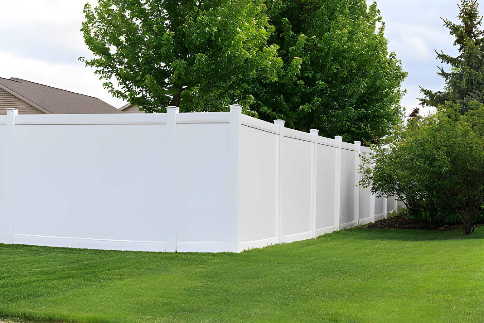 Clean white vinyl privacy fence in a green backyard.