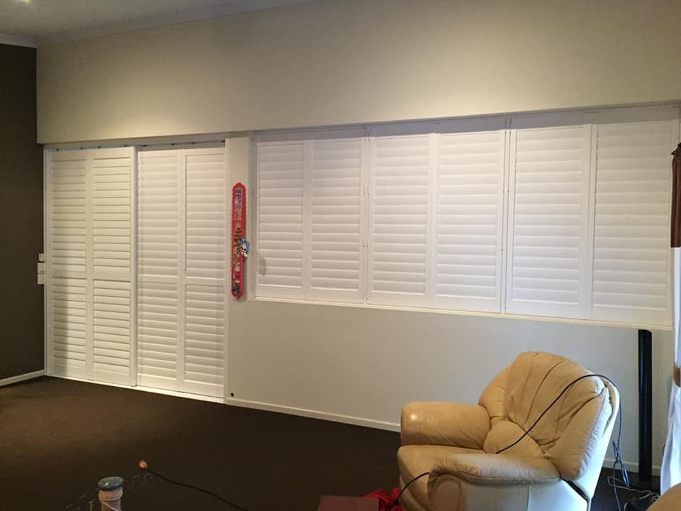 A Living Room With White Shutters on the Windows and a Chair — Whitsunday Blinds & Security in Bowen, QLD
