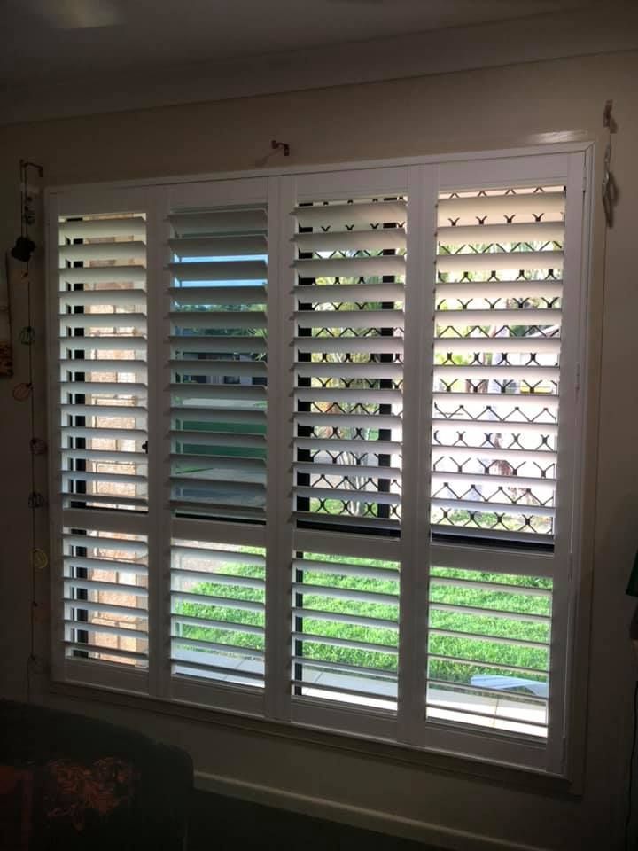 A Living Room With a Large Window With Shutters on It — Whitsunday Blinds & Security in Airlie Beach, QLD