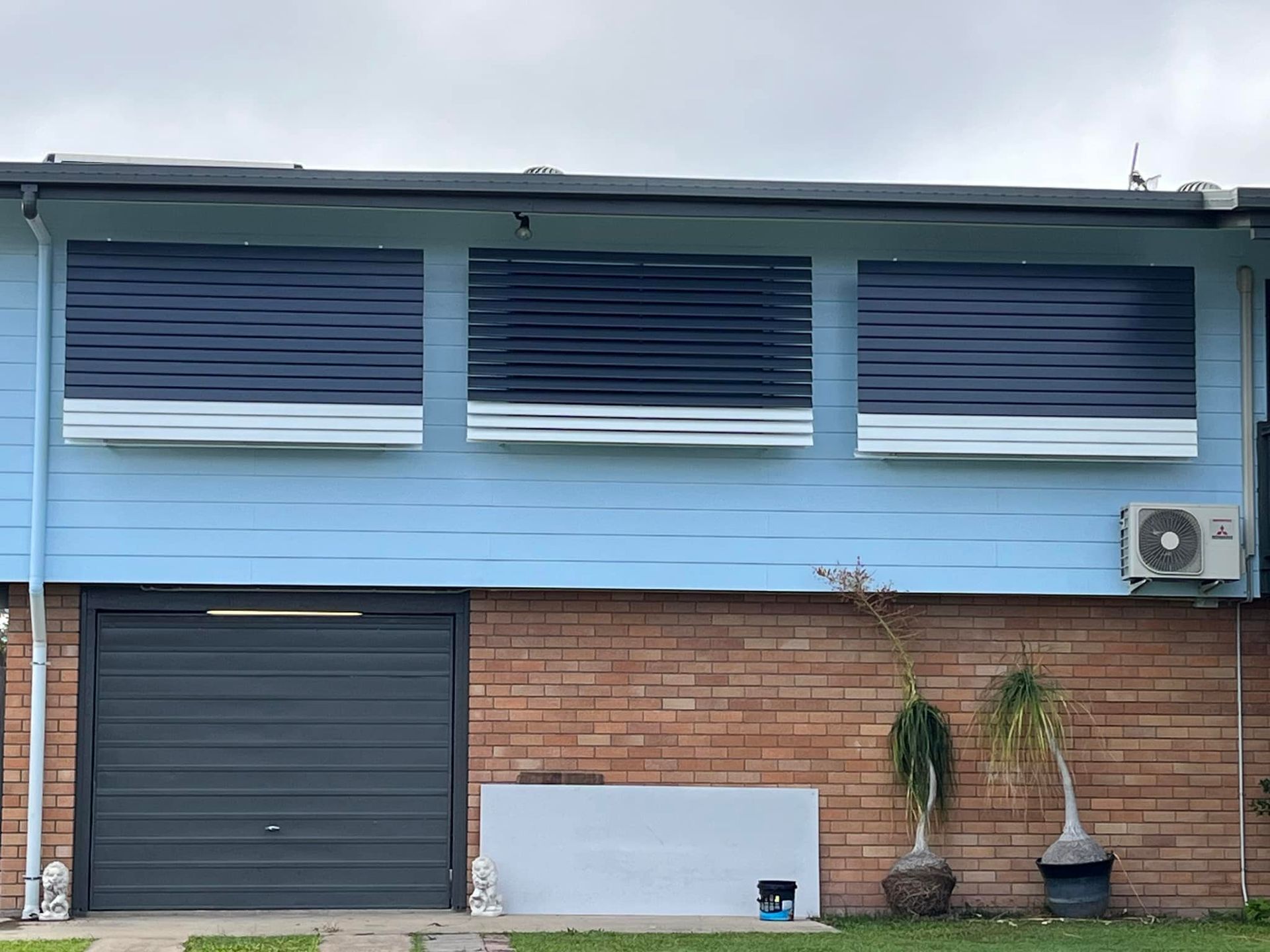A Blue House With a Black Garage Door and a Brick Wall — Whitsunday Blinds & Security In Beaconsfield, QLD