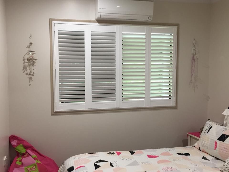 A Bedroom With a Bed and a Window With Shutters — Whitsunday Blinds & Security in Proserpine, QLD
