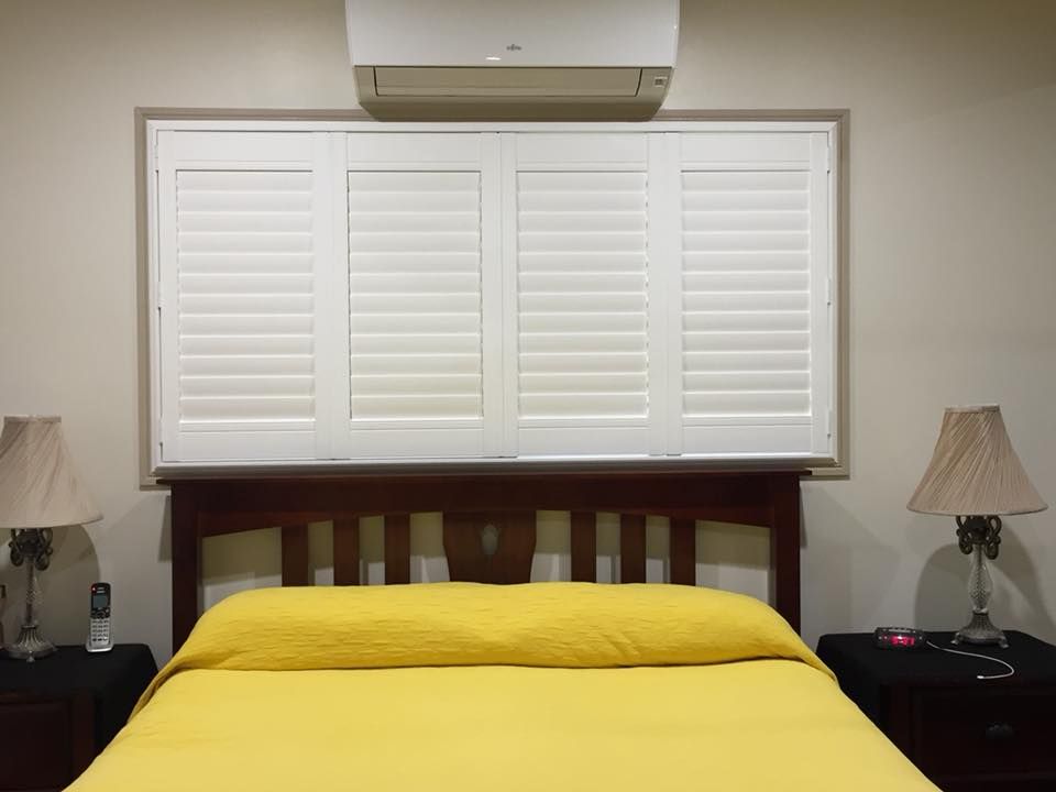 A Bedroom With a Bed and a Window With White Shutters — Whitsunday Blinds & Security in Proserpine, QLD