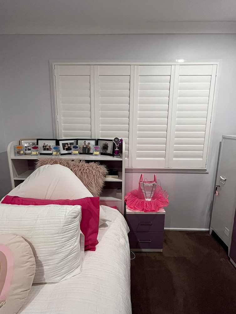 A Bedroom With a Bed, Nightstand, and Shutters on the Windows — Whitsunday Blinds & Security in Cannonvale, QLD