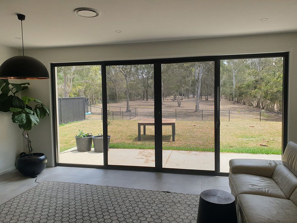 A Living Room With a Couch, Rug, and Sliding Glass Doors With Screen — Whitsunday Blinds & Security In Beaconsfield, QLD