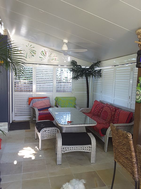 A Living Room With a Couch, Table, Chairs, And bi-fold Window Shutter — Whitsunday Blinds & Security In Beaconsfield, QLD