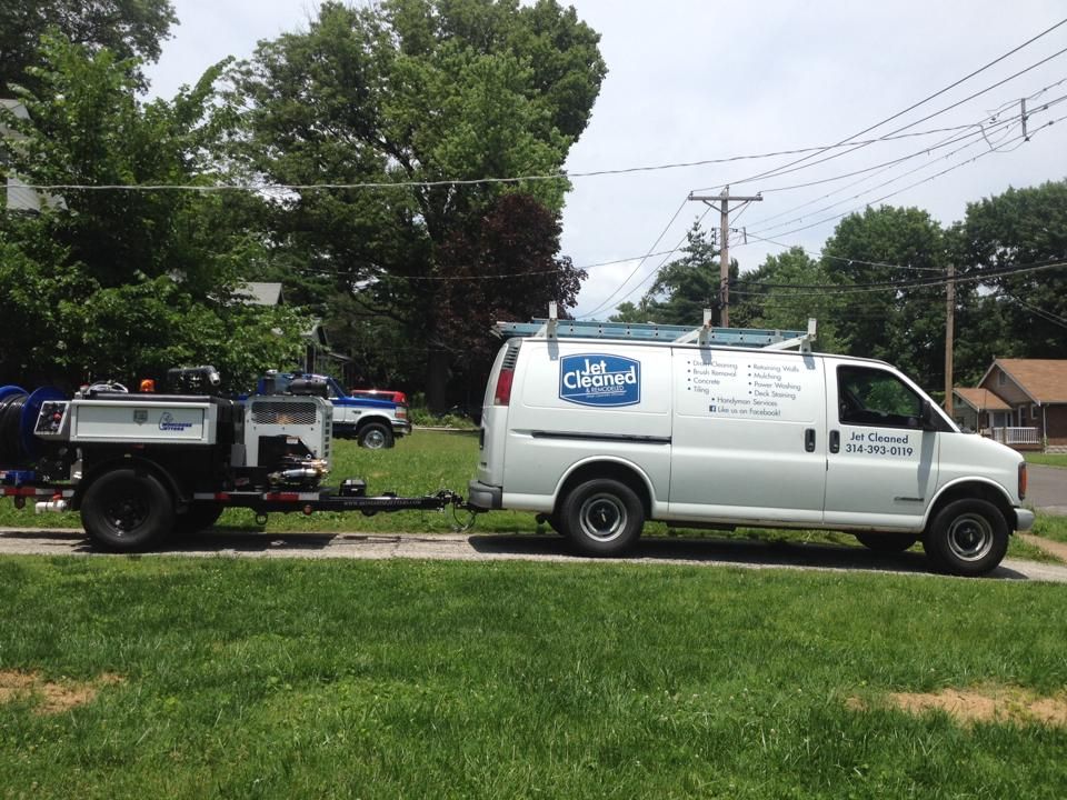 White service van towing a trailer on a grassy lawn with trees in the background.