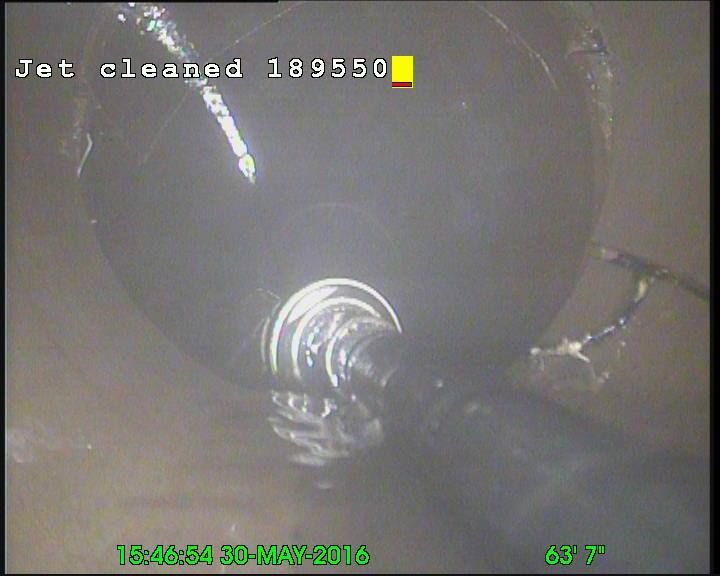 Inside a pipe, a jet cleans. Water surrounds a camera, labeled 