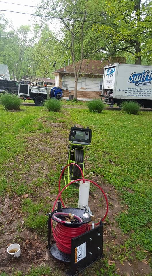 Equipment for plumbing inspection in a grassy yard, with a truck and house in the background.