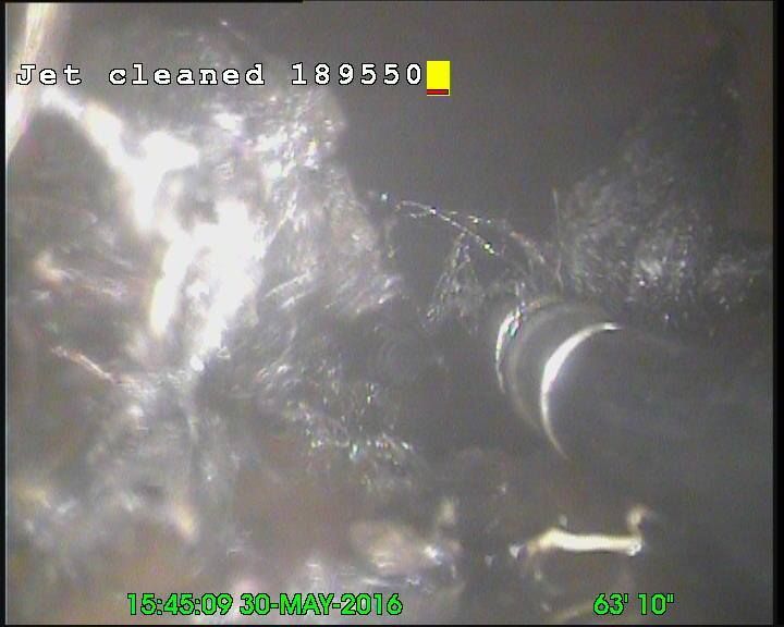 Black debris and a pipe inside a sewer line after jet cleaning.