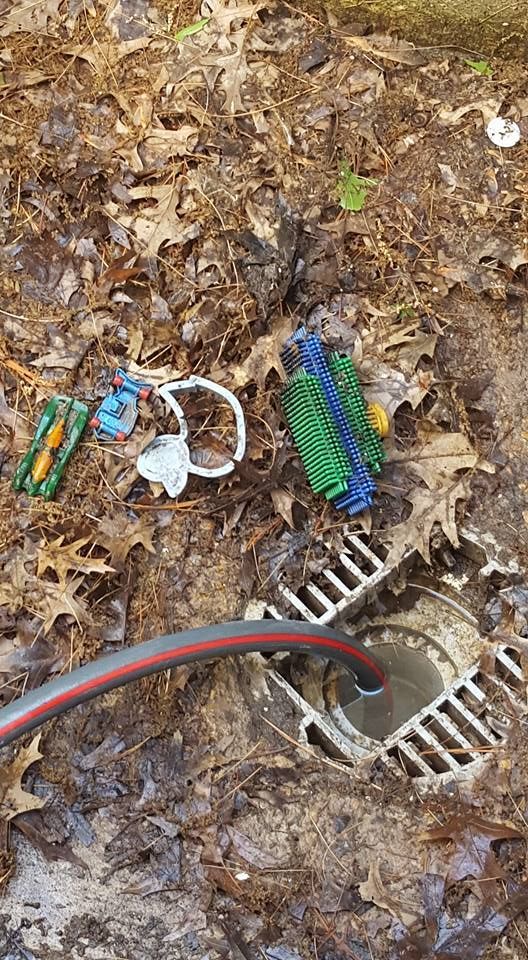 Hose pouring water into a drain in the leaves, with discarded toy parts scattered nearby.