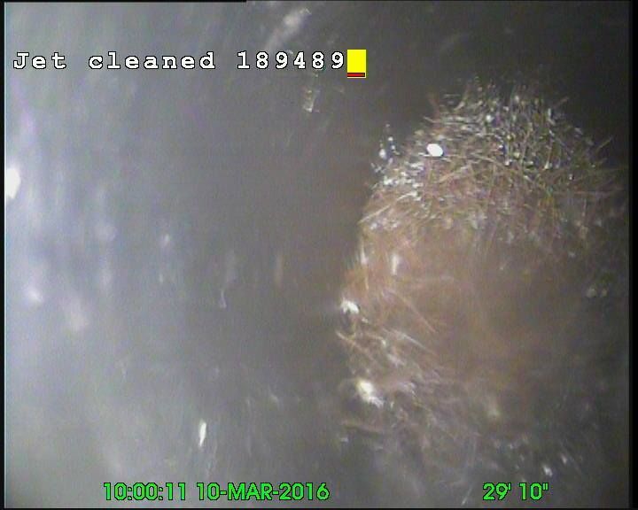 Interior view of a pipe with what appears to be a tangled mass of fibers and debris. The text 