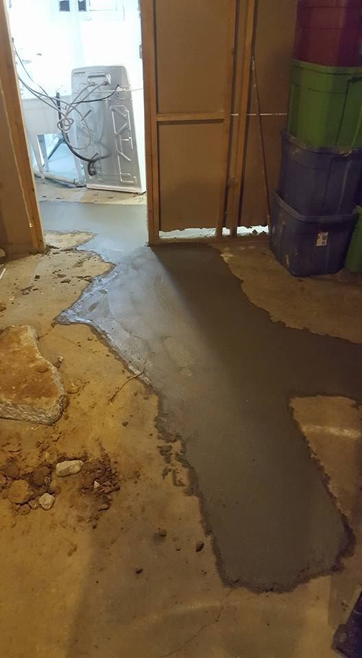 Concrete patch on a basement floor, next to a doorway, with storage bins visible.