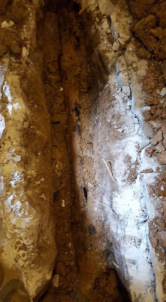 Trench dug into earth, revealing a buried pipe. Brown soil, tan and white earth sides.