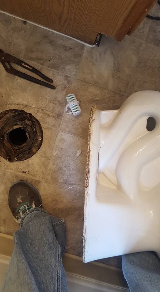 Toilet being installed next to a toilet flange on a brown floor.