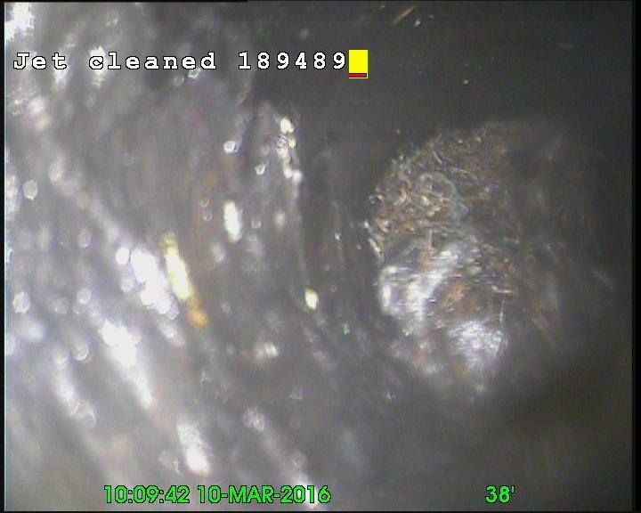 Inside a dark pipe, a camera view of debris after jet cleaning.