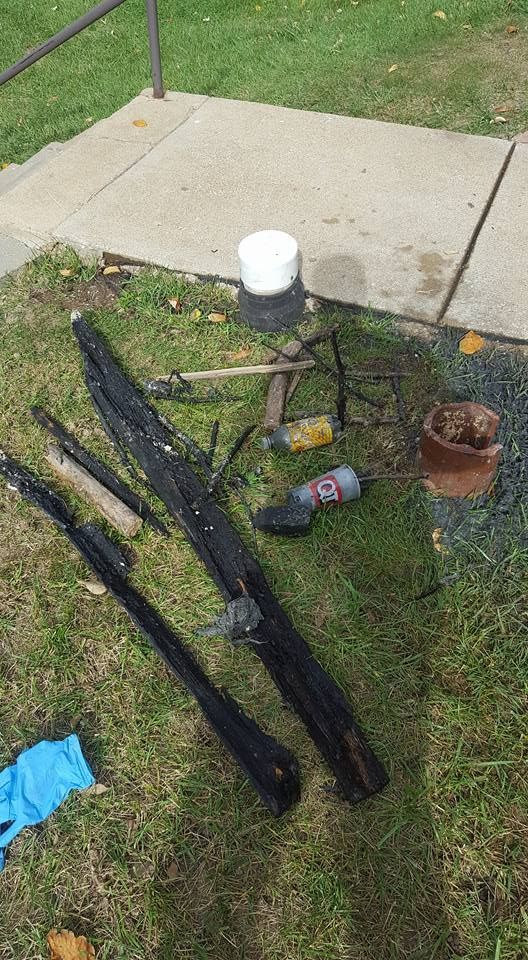 Black wooden poles and debris scattered on grass near a sidewalk.