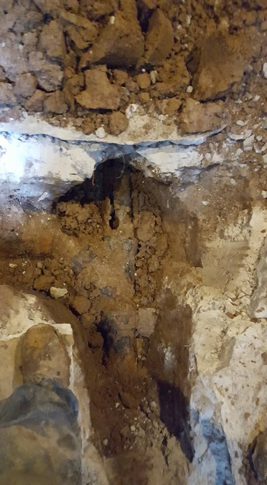 Hole in ground, revealing layers of soil and rocks. Dark, possibly wet area in the middle.