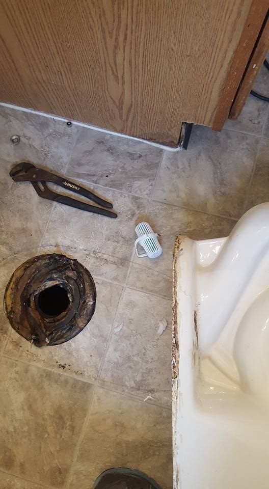 Toilet flange removed, tools and debris on floor near toilet.