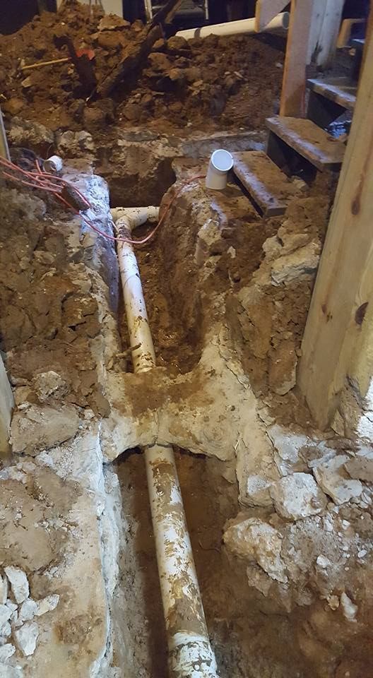 Excavated area with exposed white pipes, soil, and wooden beams.