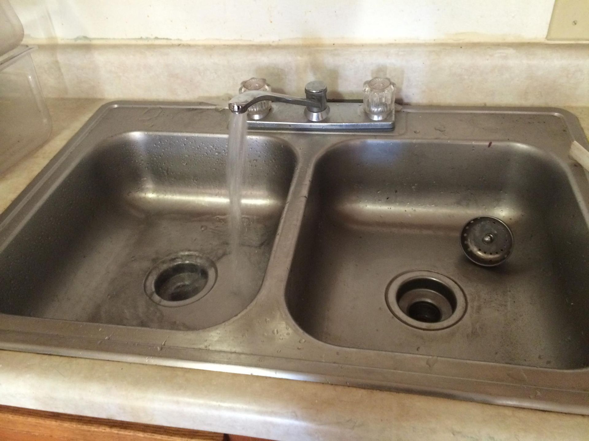 Stainless steel kitchen sink with running water; drain stopper in right basin.