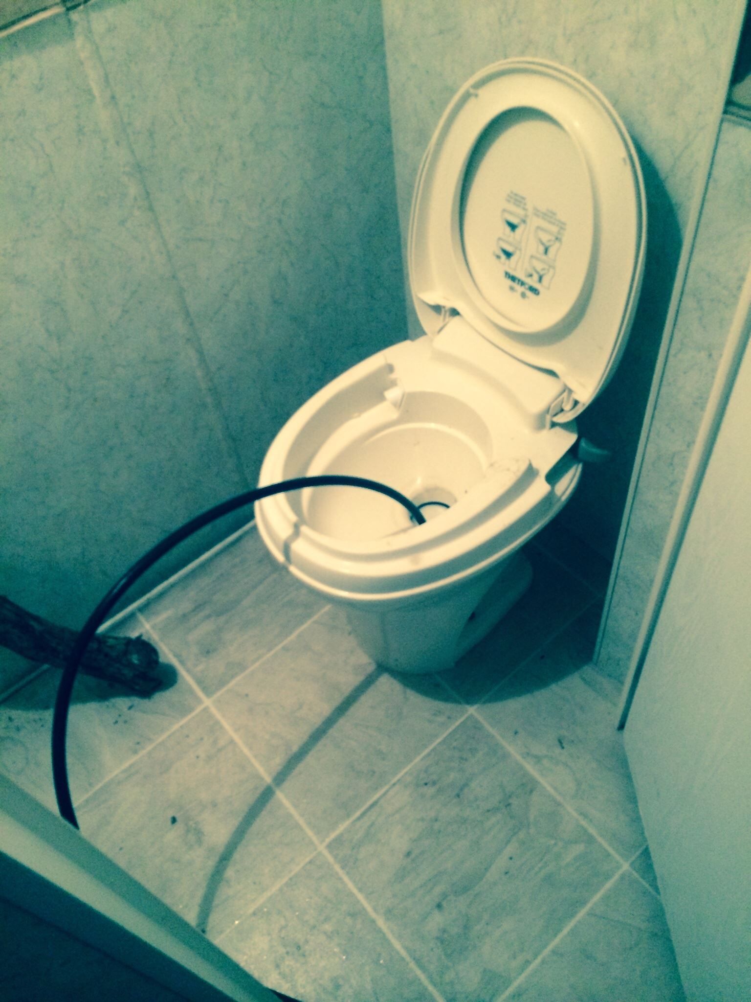 Toilet with open lid, black hose inserted, in tiled bathroom.